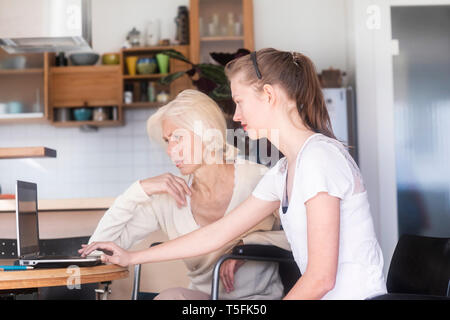 Daughter and mother in a wheelchair using a laptop Stock Photo