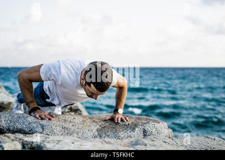 Man doing doing pushups on rock in front of the sea Stock Photo
