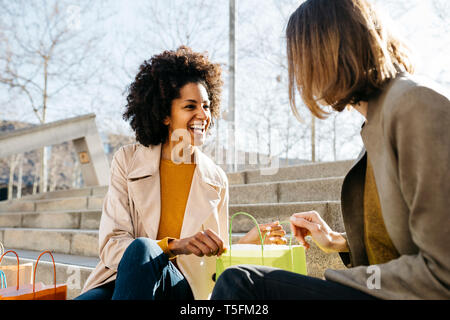 Two happy women with shopping bags sitting on stairs checking the purchase Stock Photo