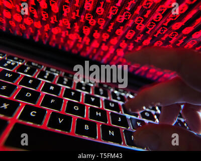 Hacker coding a computer virus infecting a laptop Stock Photo