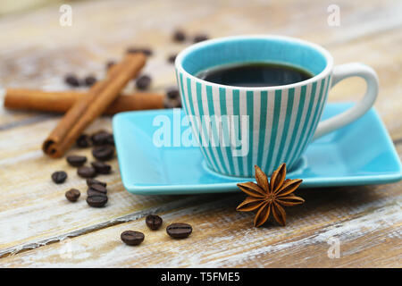 Cup of black coffee in vintage cup, star anise, cinnamon sticks and scattered coffee beans on wooden surface Stock Photo