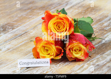 Congratulations card with three orange roses with glitter on rustic wooden surface Stock Photo