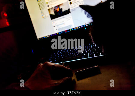 hand with a cigarette in front of a screen and a cat beside Stock Photo