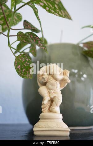 A small Ganesha figurine, next to a potted plant on a shelf. Stock Photo