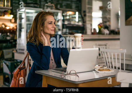 Businesswoman sitting in coffee shop, having lunch, working on laptop Stock Photo