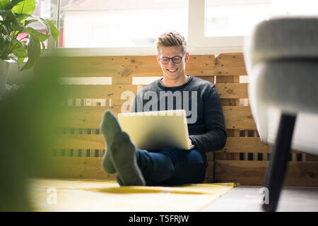 Smiling young man sitting on the floor using laptop Stock Photo