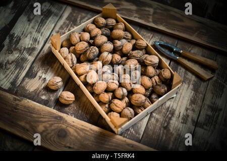 Walnuts in wooden box and nutcracker, wooden background Stock Photo