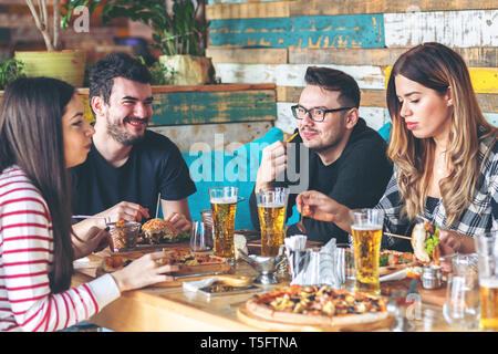 Young friends enjoying time together eating burgers and pizza at trendy pub Stock Photo