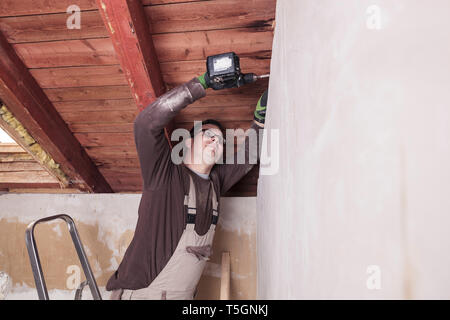 Roof insulation, worker drilling wooden board with a cordless drill Stock Photo