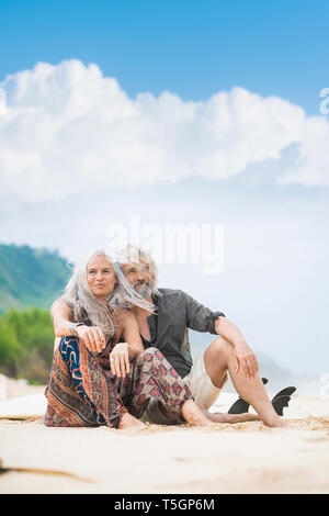 Portrait of happy senior hippie couple sitting side by side on the beach Stock Photo
