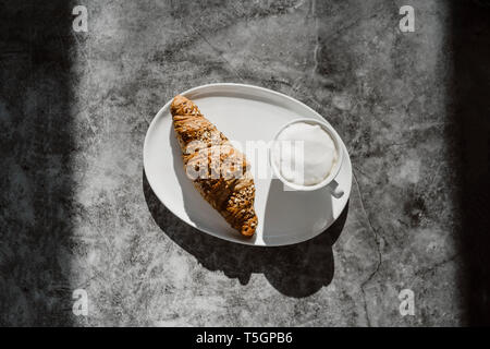 Cup of white coffee and a whole meal croissant on plate Stock Photo