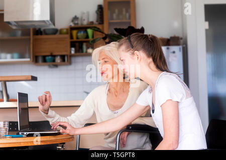Daughter and mother in a wheelchair using a laptop Stock Photo