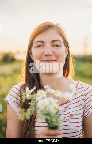 Portrait of smiling young woman holding bunch of picked wildflowers Stock Photo