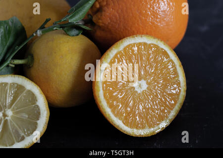 Oranges and lemons with whole and cut fruits on a dark background