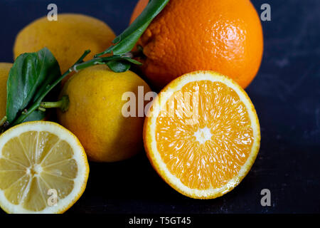 Oranges and lemons with whole and cut fruits on a dark background