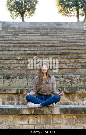 Young woman sitting outdoors on stairs doing yoga Stock Photo