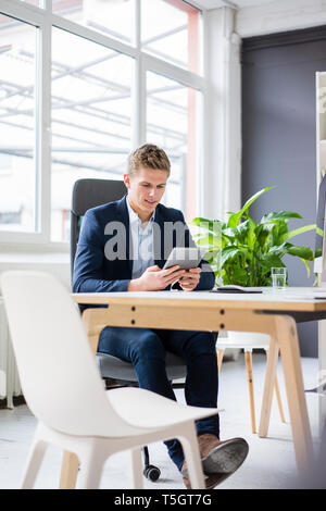 Confident young businessman sitting at desk in office using tablet Stock Photo