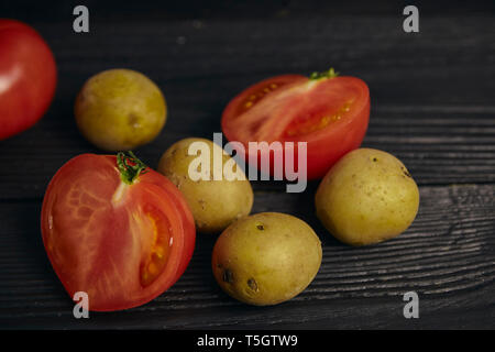 Organic baby potatoes on a wooden table with slices of red tomato. fresh vegetables. Stock Photo