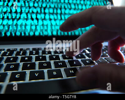 Hacker coding a computer virus infecting a laptop Stock Photo