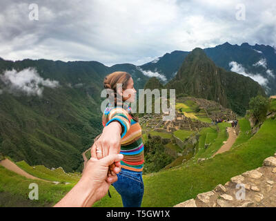 Standing couple holding hands contemplating the terraces over Machu Picchu, the most visited tourist destination in Peru. Rear view image. Stock Photo