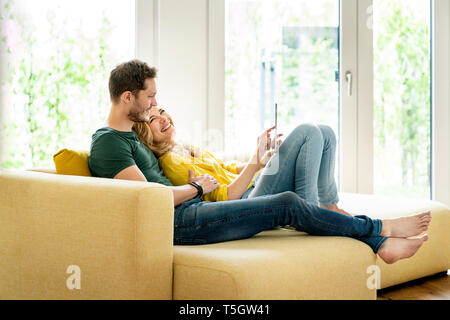 Couple sitting on couch in their new home, using digital tablet Stock Photo
