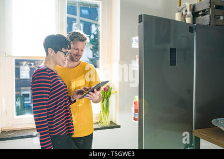 Happy couple with tablet in front of their fridge doing online shopping for groceries Stock Photo