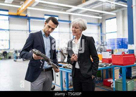 Businessman and senior businesswoman examining workpiece in a factory Stock Photo