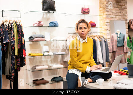 Young woman working in fashion store, using laptop Stock Photo