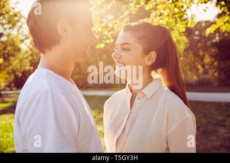Young couple smiling at each other in a park at sunset Stock Photo