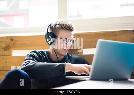 Smiling young man using laptop listening to music with headphones Stock Photo