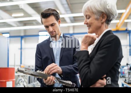 Smiling businessman and senior businesswoman examining workpiece in a factory Stock Photo