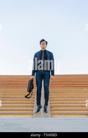 Fashionable young businessman with backpack jumping in the air Stock Photo