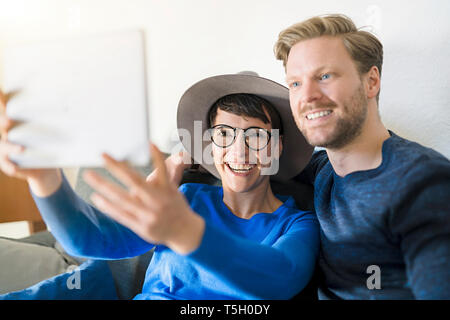 Happy casual couple taking a selfie with tablet in living room Stock Photo
