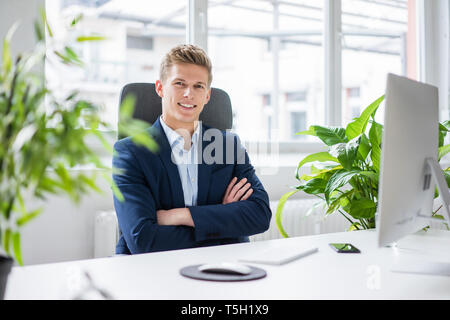 Portrait of confident young businessman sitting at desk in office Stock Photo