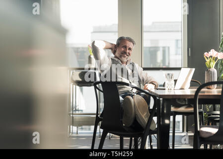Smiling mature businessman with laptop in office Stock Photo