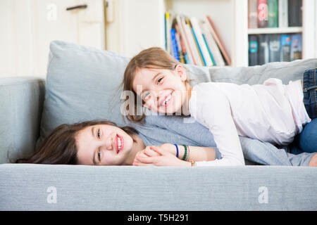 Portrait of two happy sisters cuddling on the couch Stock Photo