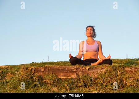 Woman meditating on a meadow in the evening Stock Photo
