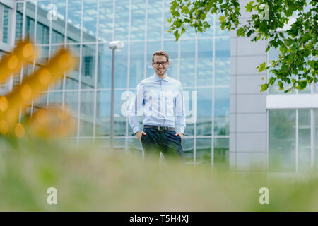 Young businessman standing in front of office buidling , smiling Stock Photo