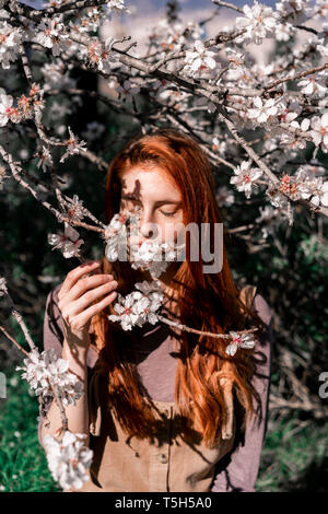 Redheaded woman smelling tree blossoms Stock Photo