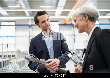 Smiling businessman and senior businesswoman examining workpiece in a factory Stock Photo