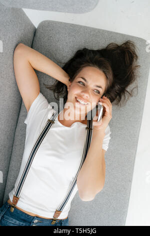 Woman lying on couch, talking on the phone Stock Photo