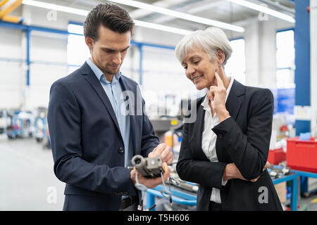 Businessman and senior businesswoman examining workpiece in a factory Stock Photo