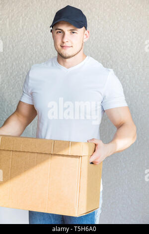 Delivery strong, muscular man loading cardboard boxes for moving to an apartment. professional worker of transportation, male loaders in overalls Stock Photo