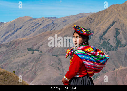 Portrait of an indigenous Quechua girl looking behind her with the Andes mountain range in the background near Cusco, Peru. Stock Photo