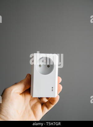 Man hand holding against gray background a new modern powerful powerline Ethernet internet adapter   Stock Photo