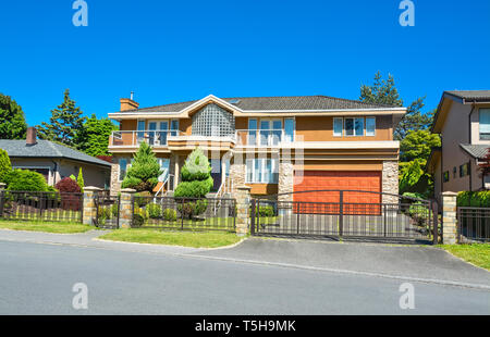 Residential house with wide garage, landscaped yard, and metal fence in front Stock Photo