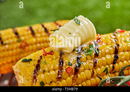 Close-up of golden corn with spices and fresh curl of butter on top grilled on grid, served outdoors Stock Photo