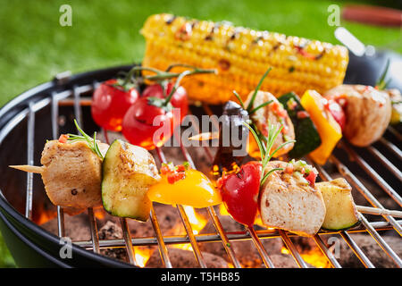 Vegetarian or vegan kebabs with tofu on the barbecue grilling over a hot fire outdoors with tomatoes and corn on the cob Stock Photo