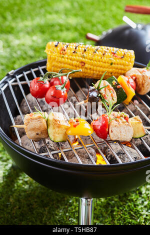 Grilling vegetables and meat kebabs on grid barbecue grill, viewed in close-up on green grass lawn Stock Photo