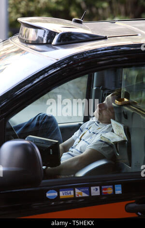 Exhausted taxi driver having getting some sleep whilst pulled over at the side of the road in his cab. London. 16.8.2010. Stock Photo